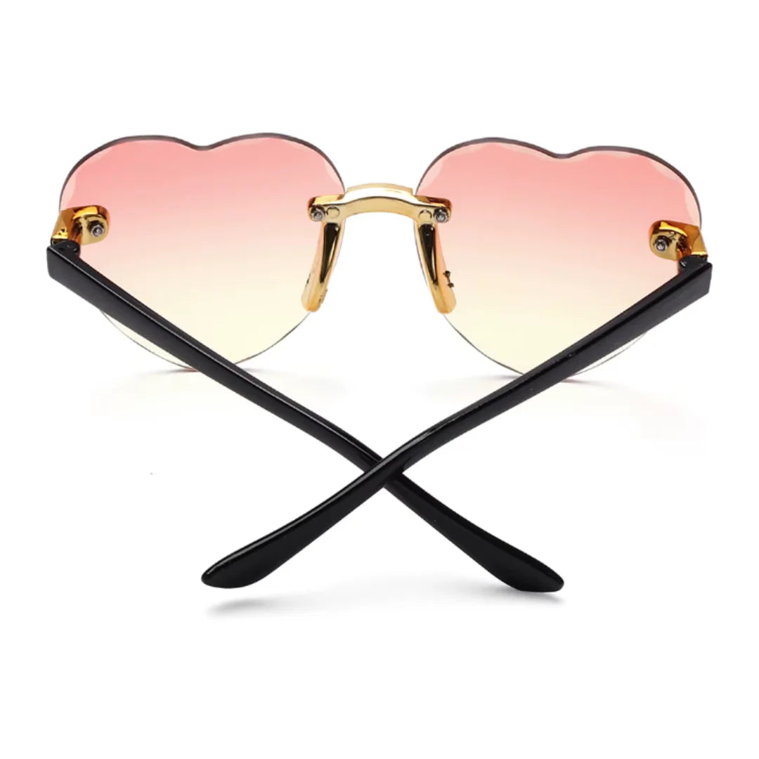 Rear view of Noémie women’s heart-shaped sunglasses in Black frame with Rose Gradient lenses, with temples crossed, on white background — polycarbonate frame, polycarbonate lenses, 100% UV protection