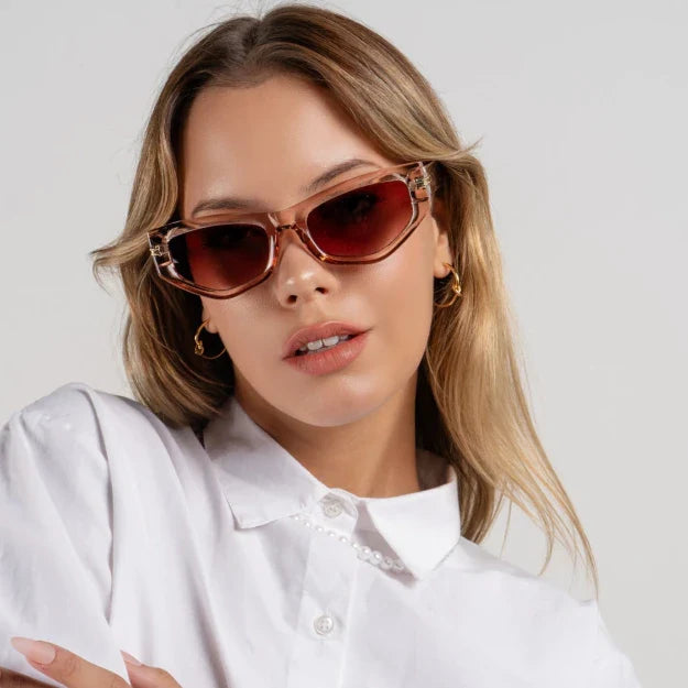 Luxe women’s cat-eye sunnies in Nude frame with Amber Gradient lenses, worn by model against white wall — model facing front with head slightly tilted left, looking at camera with a soft smile, hands not visible — acetate frame, TAC lenses, 100% UV protection