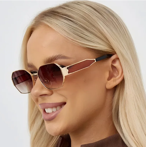 Model wearing Luna women’s retro geometric sunglasses in Gold frame with Brown Gradient lenses, in front of white wall, face turned slightly left, looking left with a smile, hands not visible