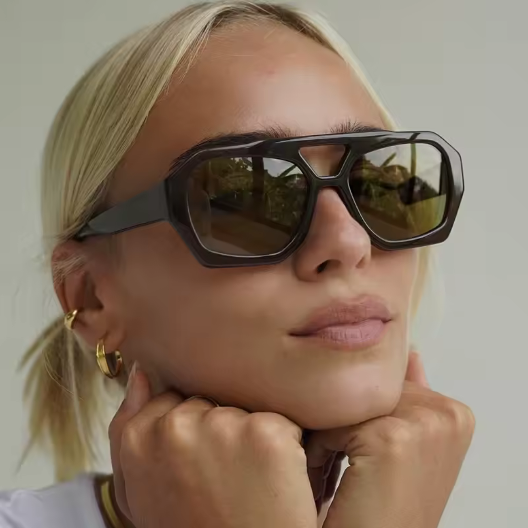 Woman wearing Ravena aviator sunglasses in Black frame with black lenses, white wall background, looking slightly to the right with chin resting on both closed fists