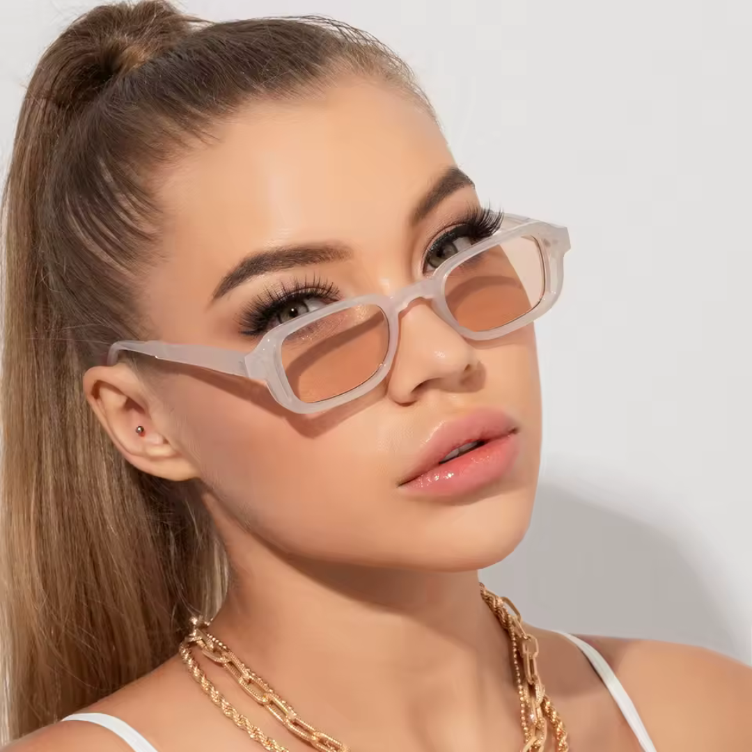 Soraya rectangular women's shades in transparent rose polycarbonate frame with soft beige acrylic lenses, 100% UV protection, worn indoors by female model against white wall, head slightly tilted left, looking at camera, hands not visible