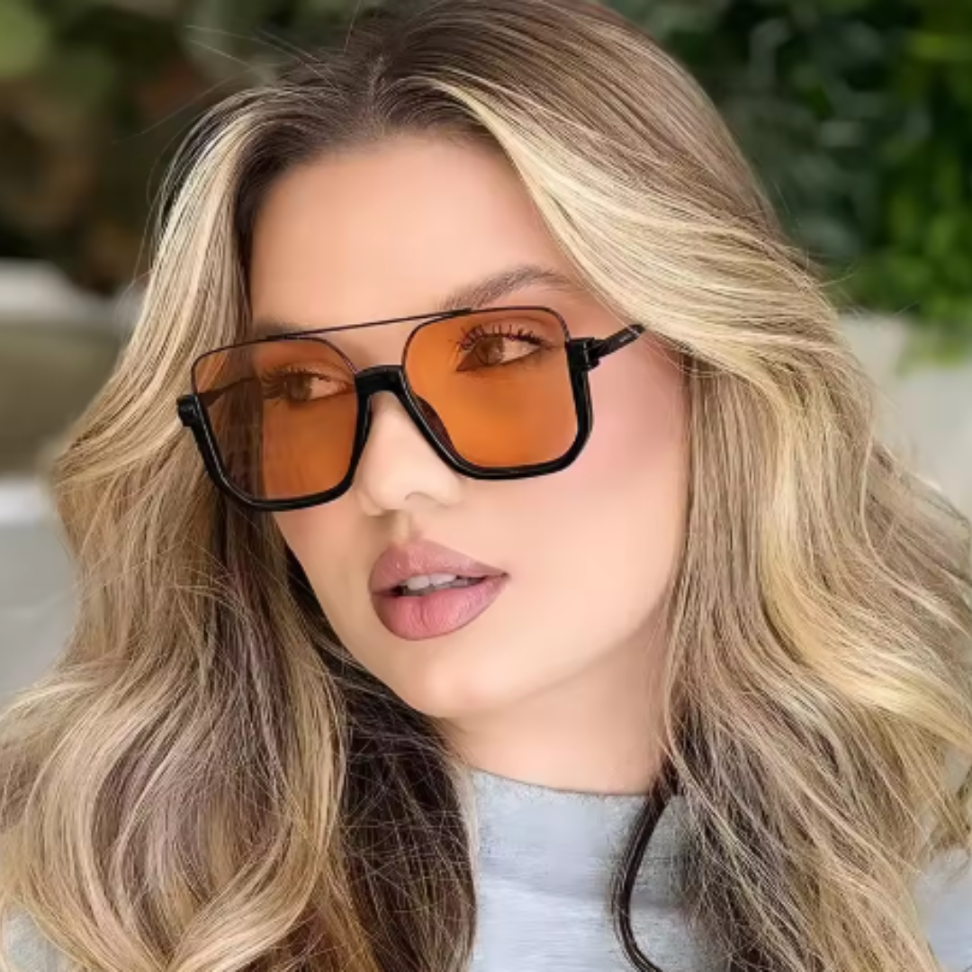 Alt text: Model wearing Opéra women's aviator-inspired square sunglasses, black lightweight metal frame with amber UV400 resin lenses, head slightly turned to the left and looking slightly left, outdoor background, hands not visible.