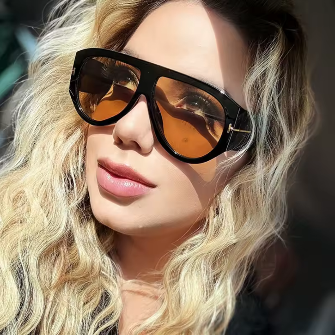Woman wearing Cannes oversized shield shades in black acetate frame with amber TAC lenses, 100% UV protection, outdoor setting, face turned slightly left looking to the left, hands not visible