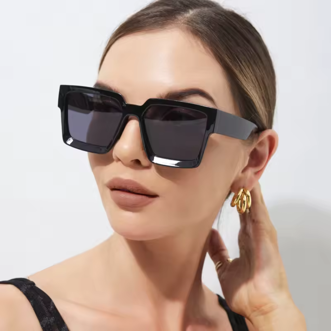 Valencia women’s square shades in Black frame with Black lenses, worn by model against white wall — model facing slightly left, looking left, right hand placed on the back of the neck — acetate frame, polycarbonate lenses, 100% UV protection