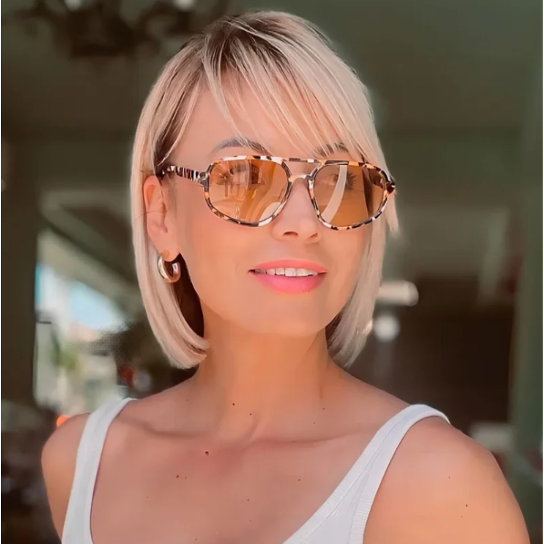 Woman wearing Brigitte aviator sunglasses in tortoise polycarbonate frame with amber acrylic lenses, 100% UV protection, outdoor setting, face turned slightly right looking to the right smiling