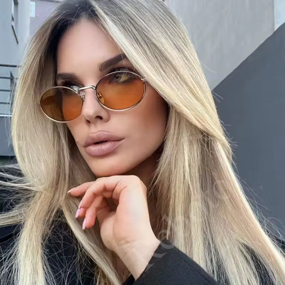 Domina women’s round shades in Tortoise frame with Brown Gradient lenses, worn by model against gray wall — model facing slightly left, looking slightly left, right hand supporting chin — metal frame, polycarbonate lenses, 100% UV protection