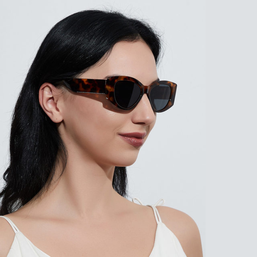 Female model wearing Aravie women’s cat-eye  shades in Tortoise frame with Black lenses, against white wall, looking to the right, hands not visible