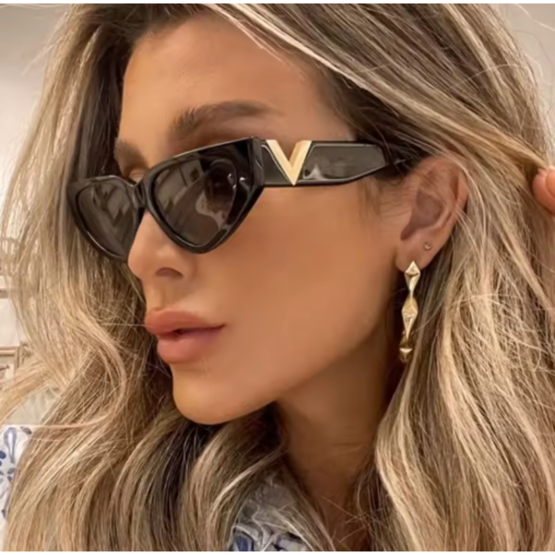 Riviera women’s cat-eye sunglasses in Black frame with Black lenses, worn by model against concrete wall — model facing slightly left, looking slightly left, hands not visible — polycarbonate frame, acrylic lenses, 100% UV protection