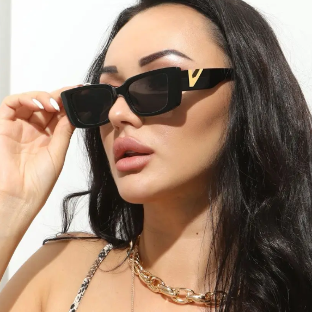 Female model wearing Celestia women’s rectangle sunglasses in Black frame with Black lenses, against white wall background, head slightly turned left, looking left, left hand touching the left temple of the frame — acetate frame, polycarbonate lenses, 100% UV protection