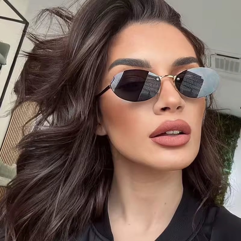 Female model wearing Velvet women’s oval  shades in Gold frame with Black lenses,  against white concrete wall, head slightly turned to the right but looking directly at the camera, hands not visible