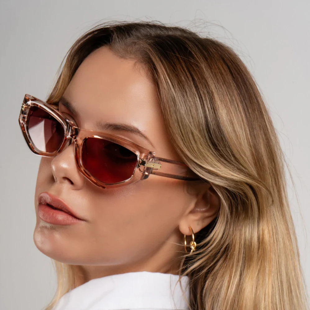 Luxe women’s cat-eye sunglasses in Nude frame with Amber Gradient lenses, worn by model against white wall — model facing slightly left, looking at camera, hands not visible — acetate frame, TAC lenses, 100% UV protection